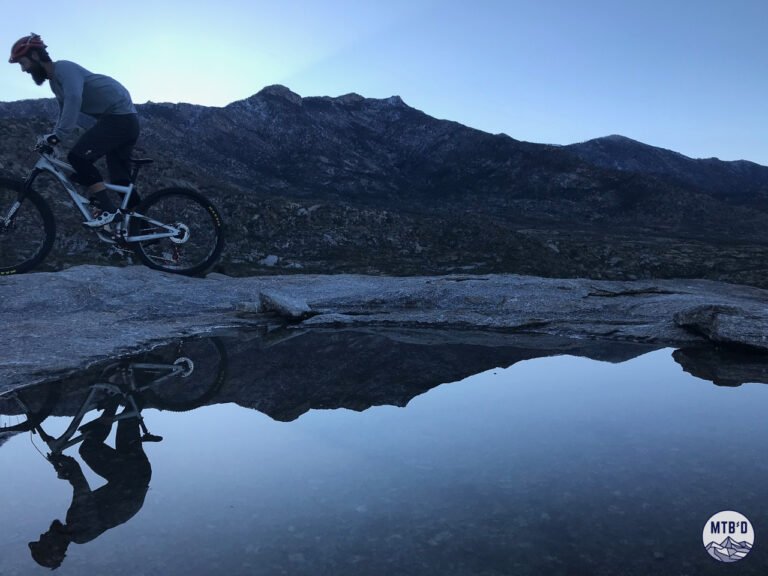 Mountain biker riding past natural reflecting pool on Cowboy Slickrock trail with Santa Catalina Mountains in background, Tucson Arizona