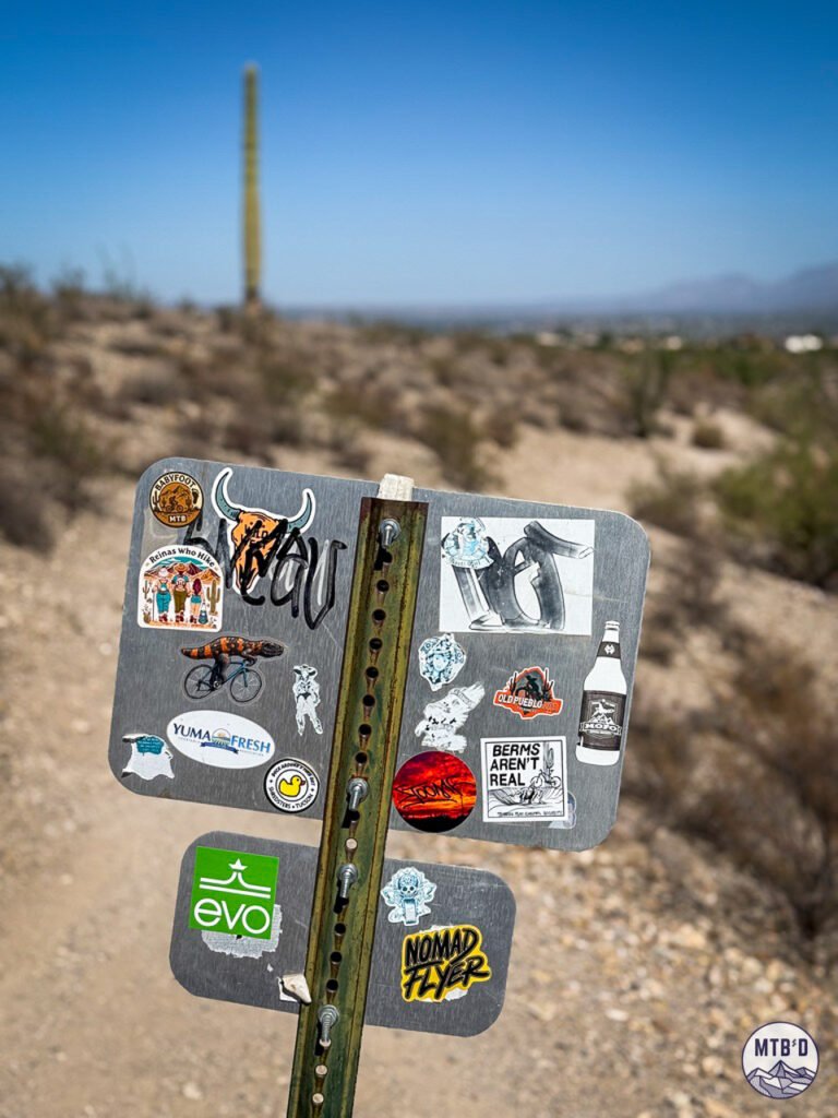 The backside of a trail sign at Sweetwater with stickers, including one that reads Berms Aren't Real