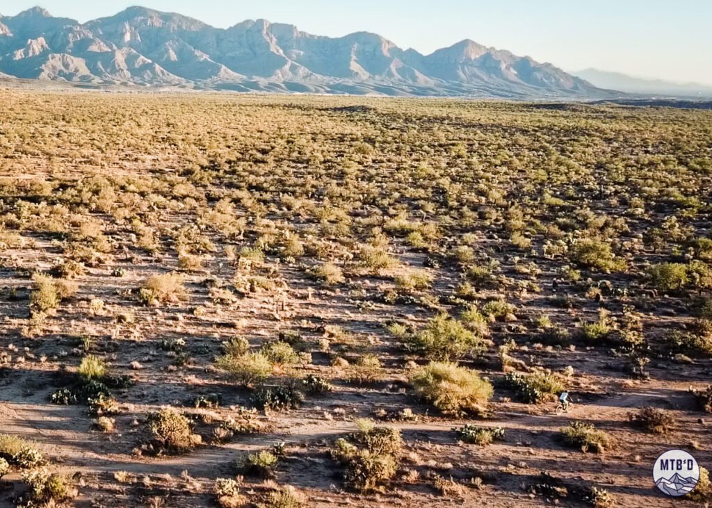 Oblique aerial drone view of mountain biker on Honeybee Canyon singletrack with Pusch Ridge in the background, Tucson Arizona