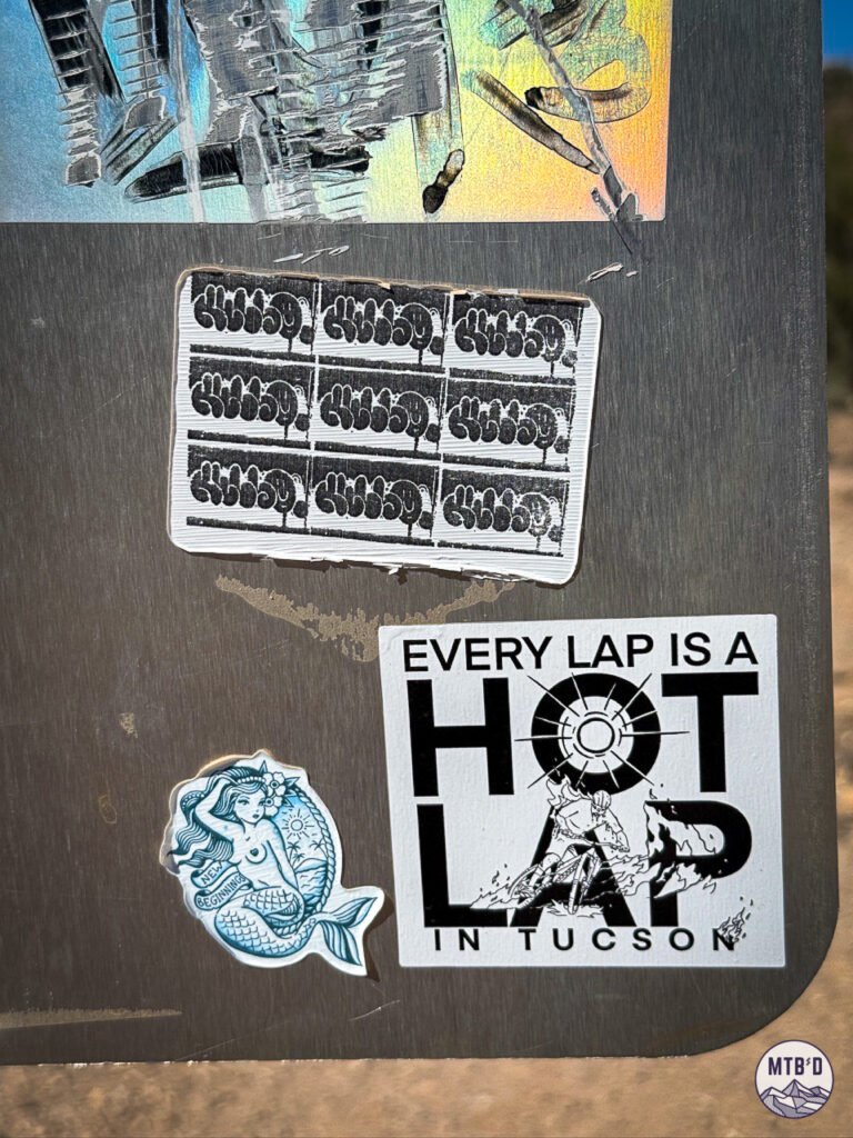 Back of trail map sign at Sweetwater Preserve Tucson with a sticker that says "Every Lap is a Hot Lap in Tucson"
